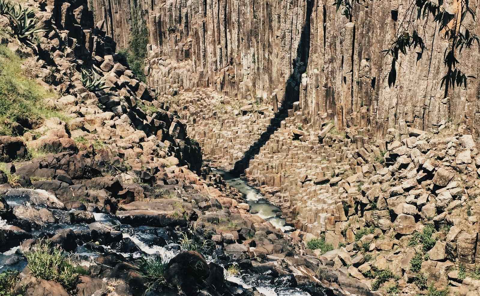 Muro de columnas basálticas con un arroyo corriendo al fondo del cañón
